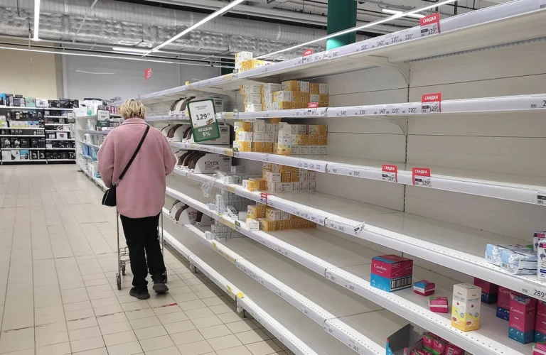 Женщина с тележкой у почти пустых полок гигиенических товаров в супермаркете