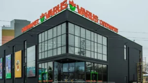 Чорна будівля супермаркету VARUS з помаранчевою вивіскою та скляним фасадом