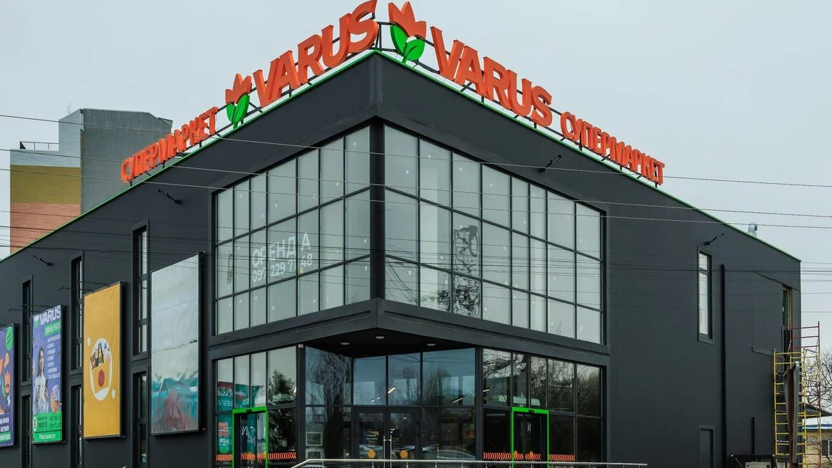 Чорна будівля супермаркету VARUS з помаранчевою вивіскою та скляним фасадом